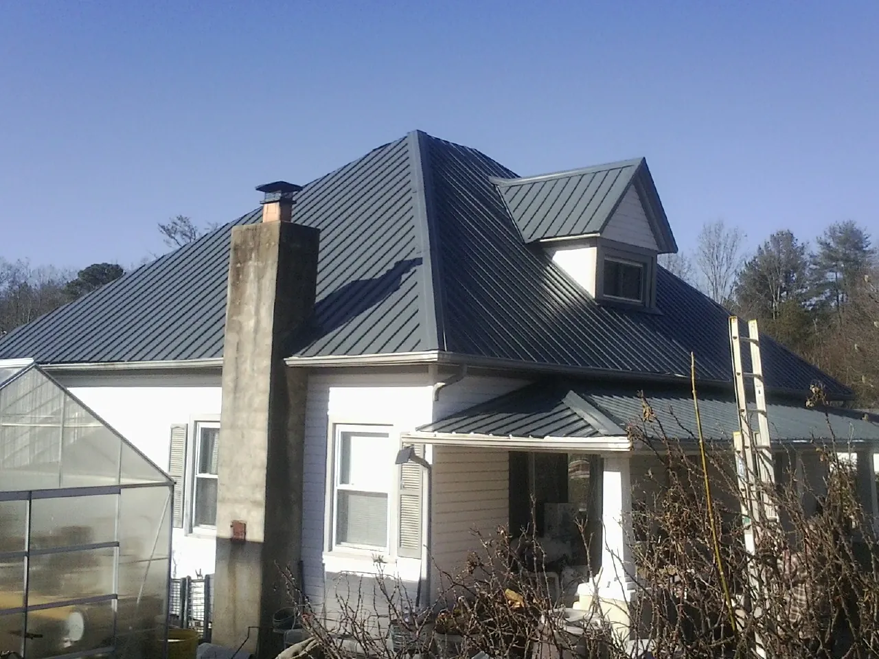 Dark blue standing seam metal roof on a white farmhouse with dormer — Slate & Tile Roof Repair by Roofing Brothers in Deweyville