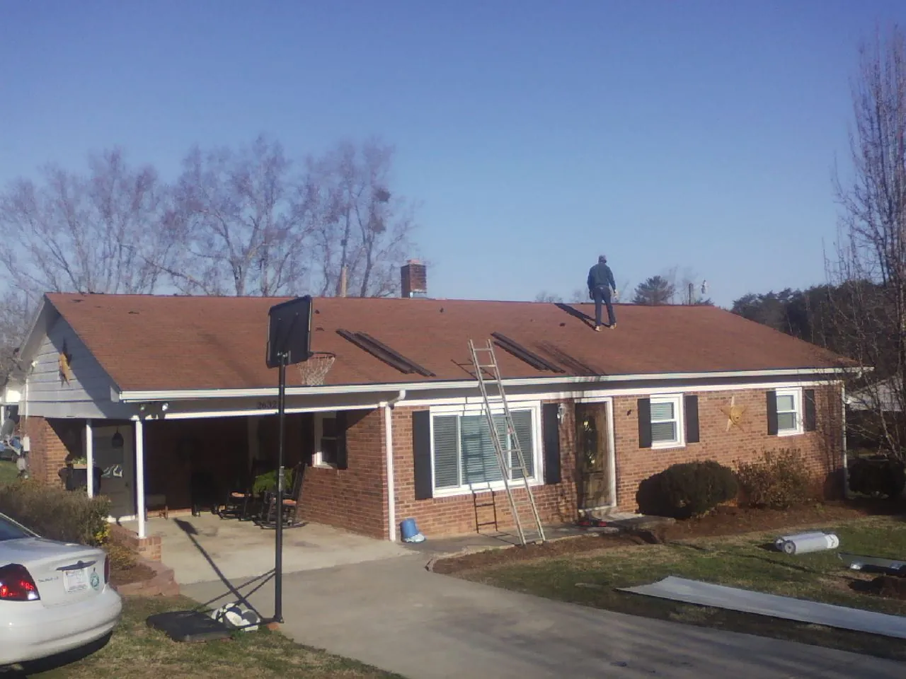 Roofer stripping a shingle roof on a brick ranch before metal panels in Deweyville