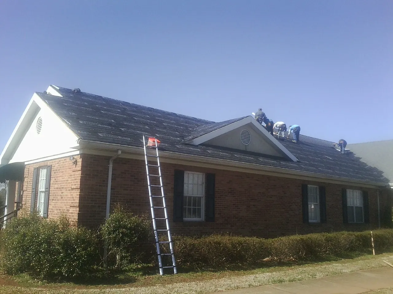 Crew tearing shingles off a brick ranch roof with a ladder set — Metal Roof Repair work by our crew in Deweyville