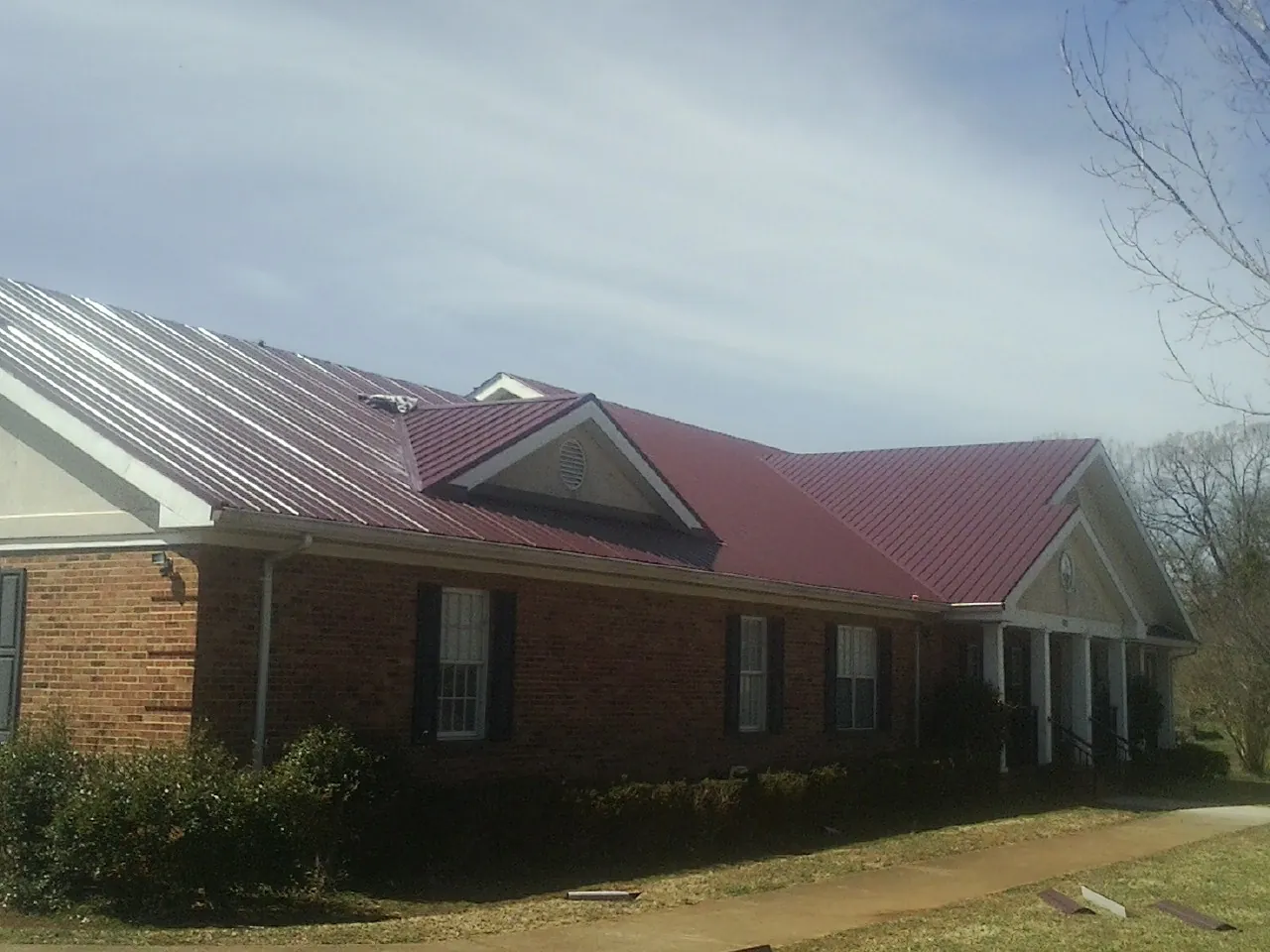 Red metal roof with gabled entries on a long brick building, from a Hail Damage Roof Repair job in Deweyville