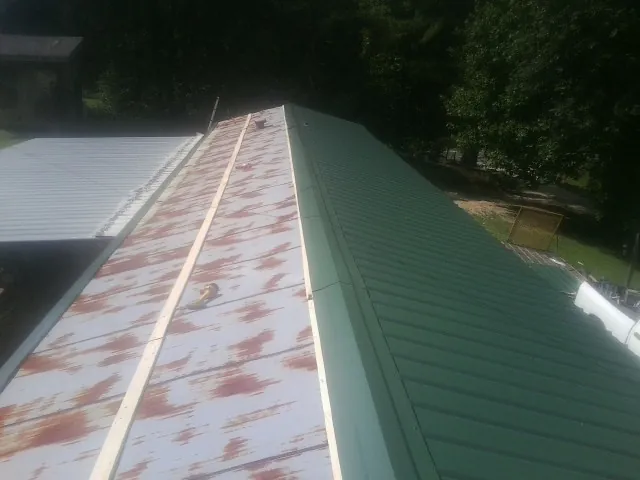 Old rusted panels beside newly installed green metal roofing — Wind Damage Roof Repair by Roofing Brothers in Deweyville