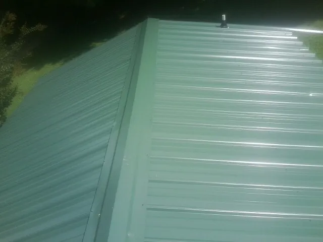 New green metal panels meeting at the ridge of a roof — Flat Roof Repair work by our crew in Deweyville