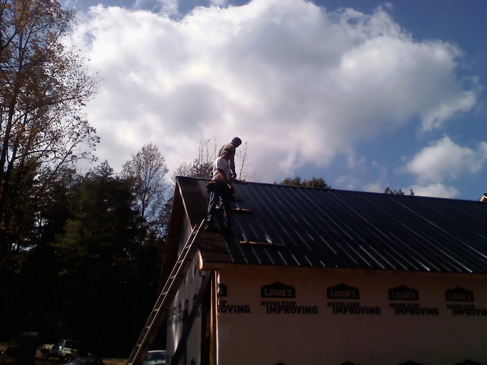 Roofer fastening dark metal panels high against a cloudy sky, from a Roof Inspection job in Deweyville