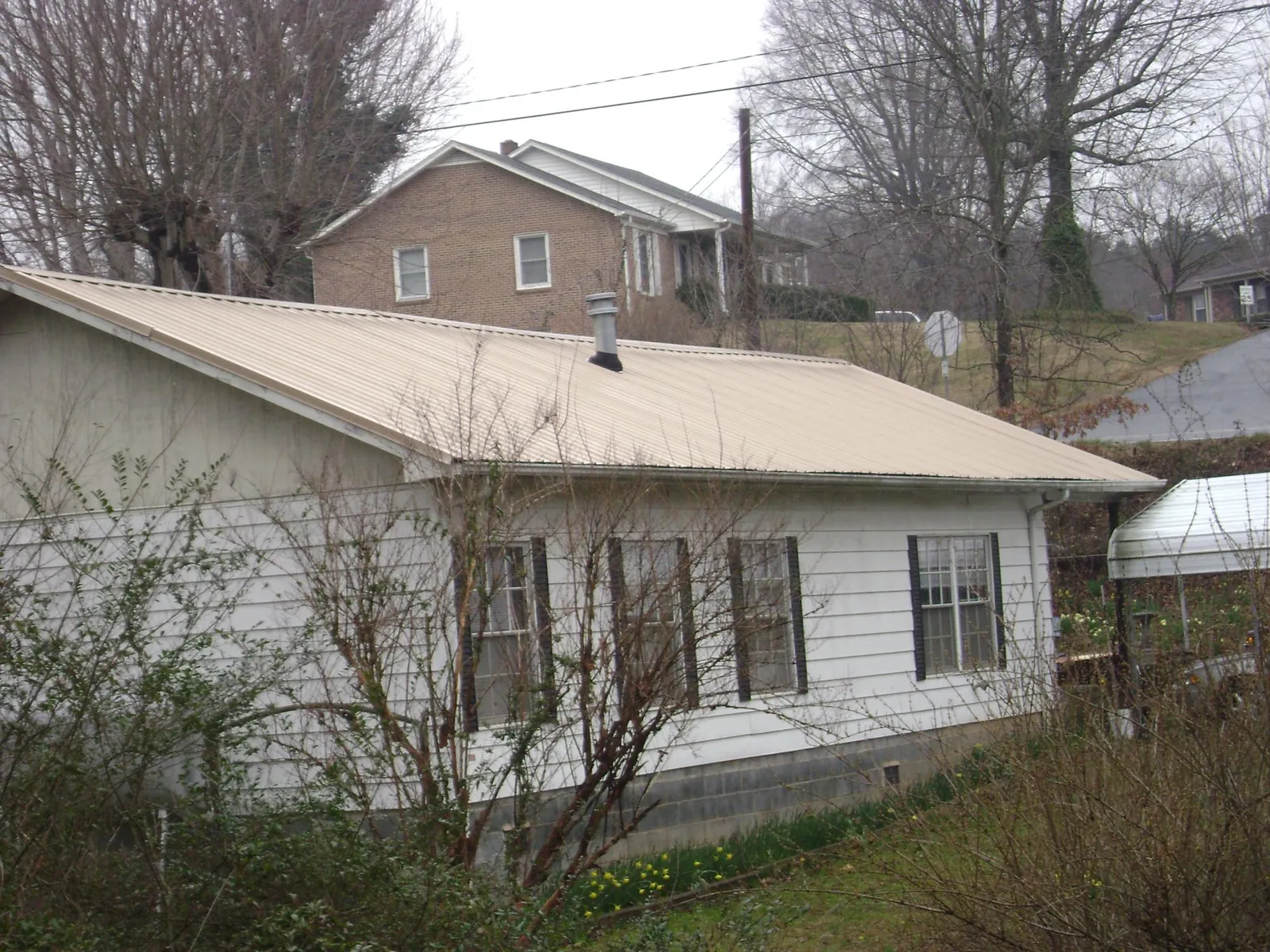 Tan metal roof on a white sided house set into a hillside — Commercial Roofing by Roofing Brothers in Deweyville