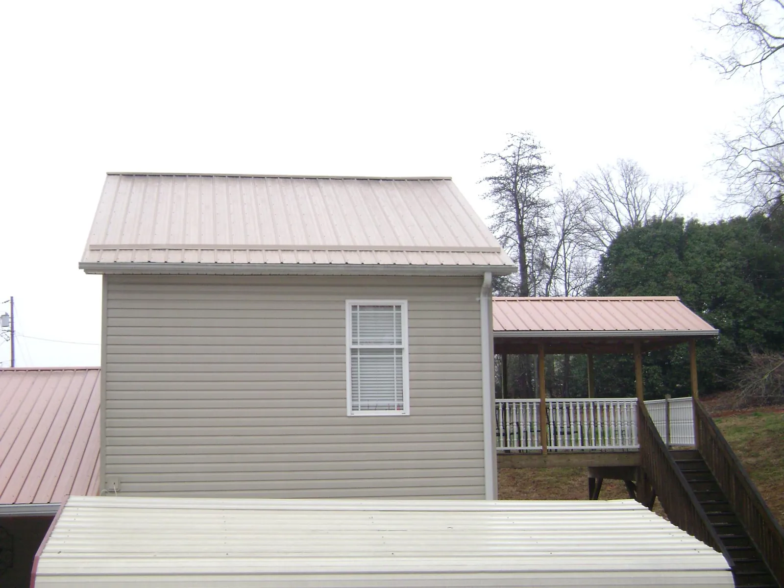 Tan metal roofs on a two story addition and attached porch, from a Roof Replacement job in Deweyville